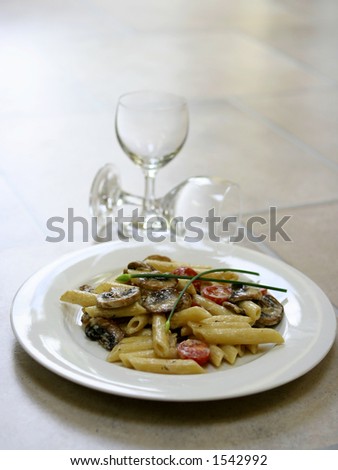 A plate of mushroom pasta and cream with tomatoes and two empty wine glasses