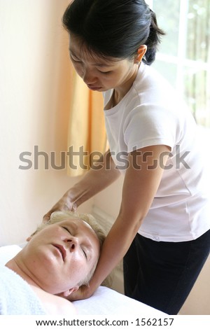 A massage therapist giving a head massage to a client as part of a holistic massage