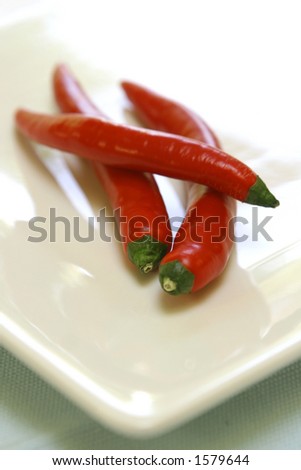 Three slender red chillies arranged on white plate
