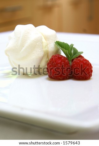 A double cup of meringue filled with cream on a plate with three raspberries as decoration