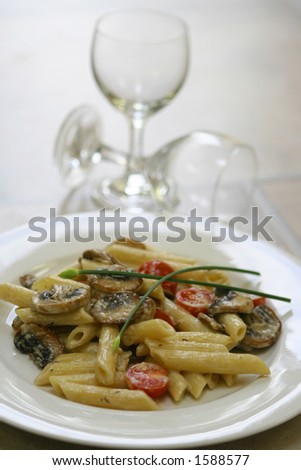 A plate of mushroom pasta with tomatoes and two empty wine glasses