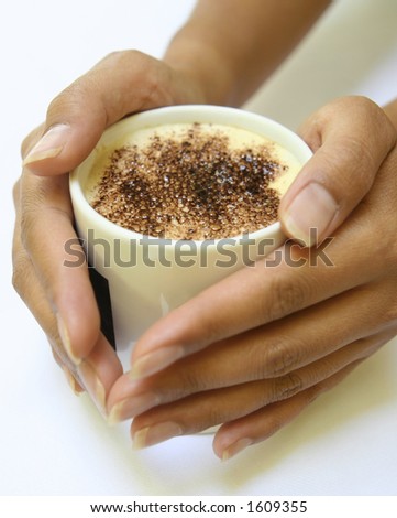 Feminine hands gently holding a mug of hot cappucino coffee with chocolate sprinkle on top