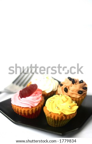 Four mini cupcakes of assorted decorations on black plate, isolated with copy space