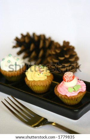 Three mini cupcakes of assorted decorations on black plate, isolated with copy space