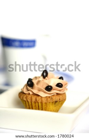 One mini cupcake with a cup of coffee on the side isolated on white