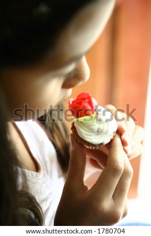 A young girl about to eat her little mini cupcake with rose biscuit
