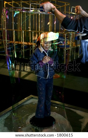 A young girl stands in the middle of a soap tray, with huge soap bubble encircling her
