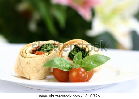 A plate of mozzarella and spinach tortilla wrap sandwich with cherry tomatoes