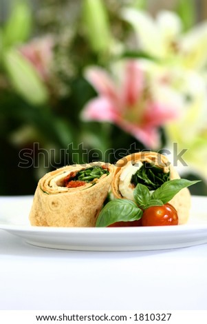 A plate of mozzarella and spinach tortilla wrap sandwich with cherry tomatoes and basil leaves