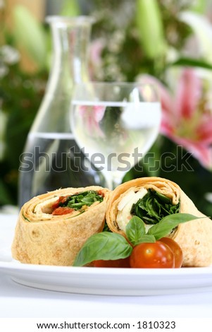 A plate of mozzarella and spinach tortilla wrap sandwich with cherry tomatoes and a glass of water