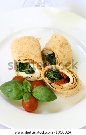 A plate of mozzarella and spinach tortilla wrap sandwich with cherry tomatoes