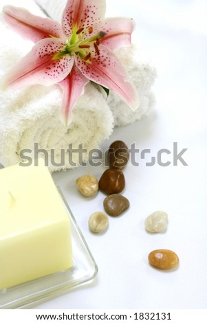 A setting for a spa consisting of white towels, a candle, therapy stones and a lily on white