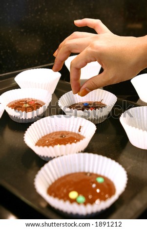 Lady\'s fingers placing chocolate sprinkles on muffin mix, ready for the oven.