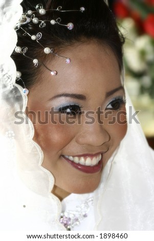 A bride in white with white scarf smiles happily on her wedding day.