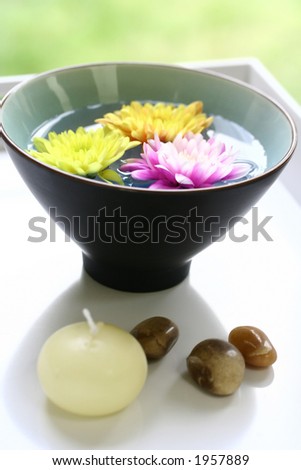 A bowl of floral scented water with candle and therapy stones on white. Suitable for relaxation therapy and spa treatment.