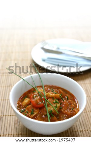 A bowl of freshly cooked king prawn masala on bamboo mat, with copyspace