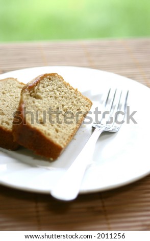 Two slices of banana loaf cake on white plate, on bamboo mat.