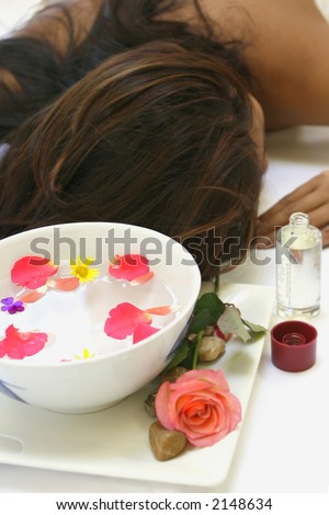 A woman awaits a sensual body massage with a bowl of floral scented rosewater and massage oil.
