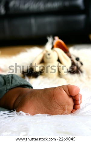 A baby's foot as he lays asleep on sheep skin rug with some baby toys in background.