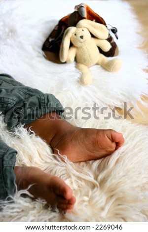 A baby's foot as he lays asleep on sheep skin rug with some baby toys in background.