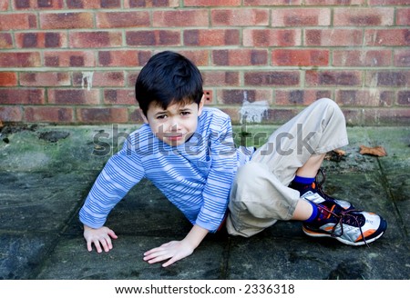 A young boy slips over and falls on his bottom.