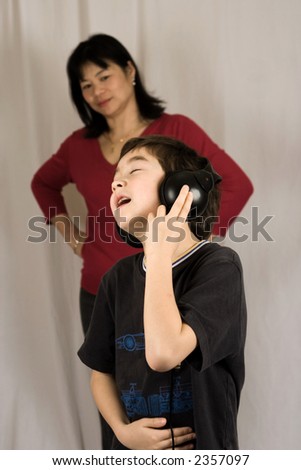 A boy listening to his music on the headphone, oblivious to his mother in the background.