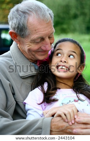 A little girl having fun with her grandfather, outdoors in summer. Concept of love and diversity.