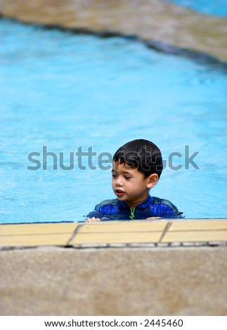 A young boy in an all-in-one swimsuit in a swimming pool in the tropics.