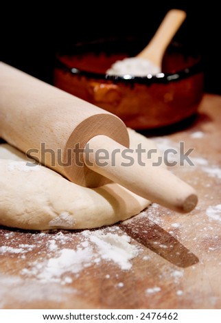 Rolling pin on dough with scattered flour and bowl of flour in background.