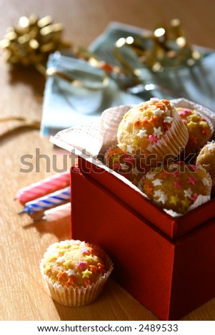 A box full of mini star fairycakes as individual birthday cakes to be shared, three candles in the background.
