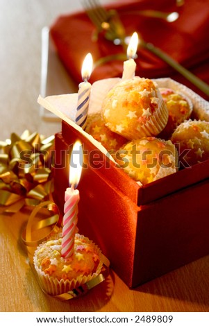 A box full of mini star fairycakes as individual birthday cakes to be shared, three symbolic candles lit up.