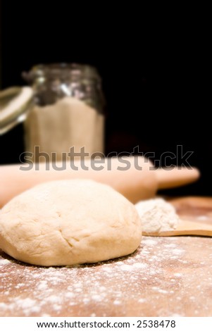 Ball of kneaded dough, rolling pin with scattered flour and jar of flour in background.