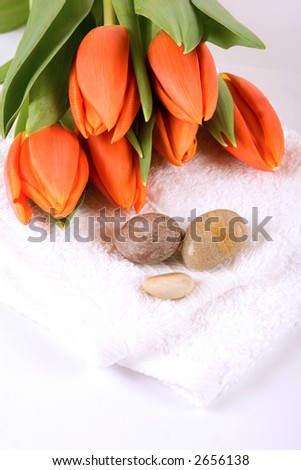 Fresh orange tulips on white towels and polished pebbles as part of alternative healthcare or spa setting.