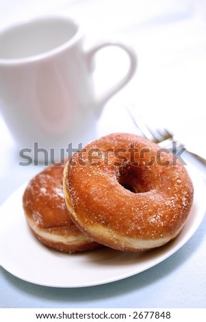Two delicious sugared ring donuts served on white plate with a cup of hot drink on the side.