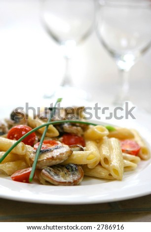 Plate of mushroom pasta with cream and tomatoes on white plate.