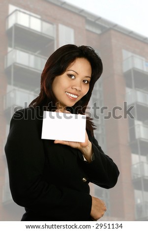 Female agent/businesswoman holding a white card for own insertion of text with modern building in background.