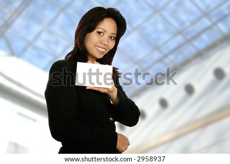 Asian businesswoman holding white card for insertion of text, with modern building interior in background. Room for copyspace.