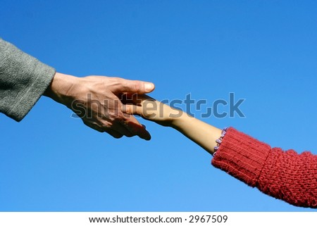 Young child\'s hand reaching out towards an adult, shot against beautiful blue sky.