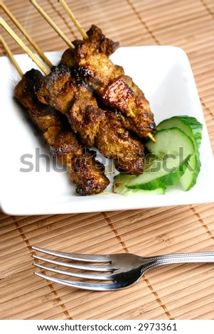Plate of hot steaming satay ( grilled spiced meat ) served with slices of cucumber.