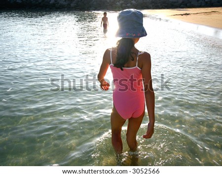 A young girl wades through the clear calm water of the sea in the late afternoon.