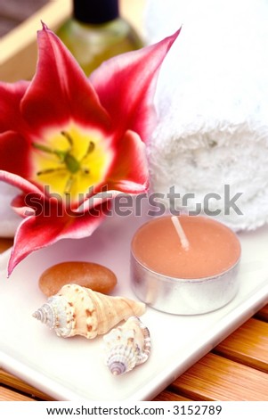 Spa setting made up of candles, white towel and pebbles on white.