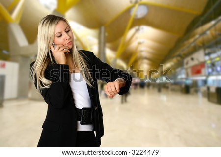 Businesswoman looking at her watch while being on the phone, standing in the departure hall of an airport, waiting to catch her flight for her business travel.
