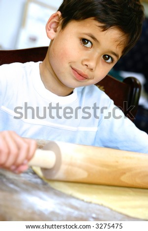 A young boy helping his mom in the kitchen at making cookies, showing him rolling dough with a rolling pin.