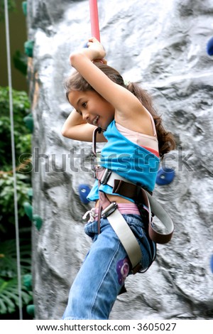 Young girl being lowered down by the safety rope from the indoor rock climbing activity.