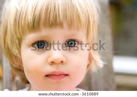 Curious little girl toddler with deep blue eyes, curious, looking at viewers, on an outdoor setting.
