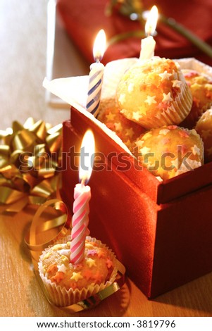 Boxed of mini cupcakes with sugar stars and burning candles.