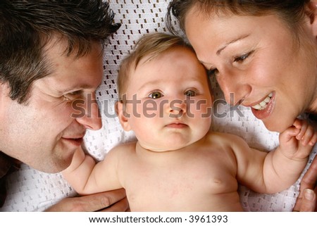 Young mother and father playing with beautiful baby girl, on soft white blanket.