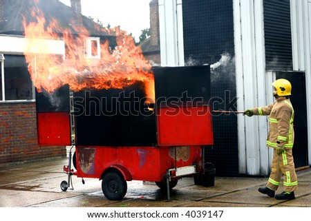 Fireman simulating a kitchen fire by pouring a bowl of water onto a very hot pan showing how it catches fire instantly.