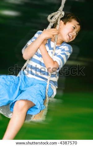 Young boy having fun in the outdoor swing in the garden.