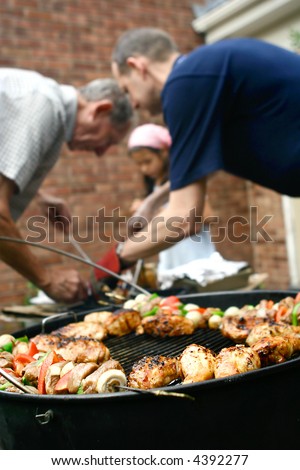 Family having a barbecue in the garden, helping each other out with the food preparation.